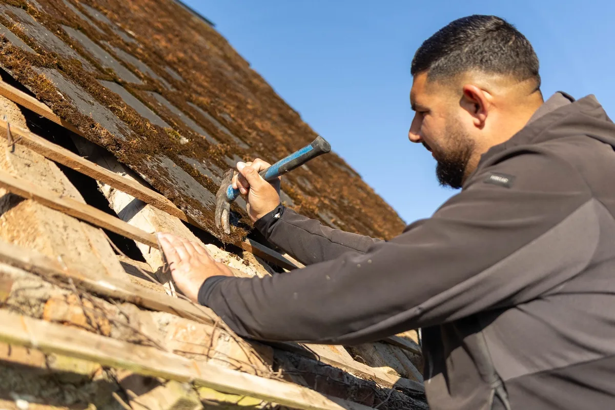 Charpentier KING RENOV travaillant au marteau sur une charpente en bois